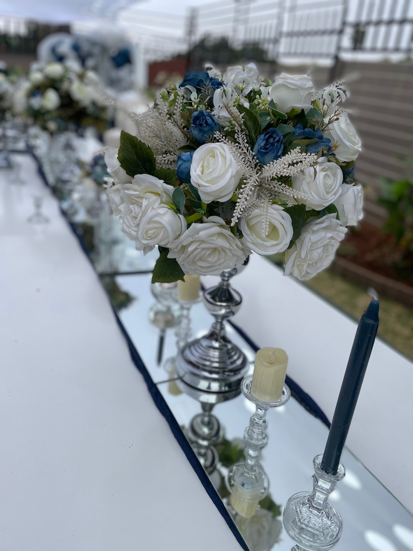Elegant floral centrepiece with white and blue roses on a mirror table runner